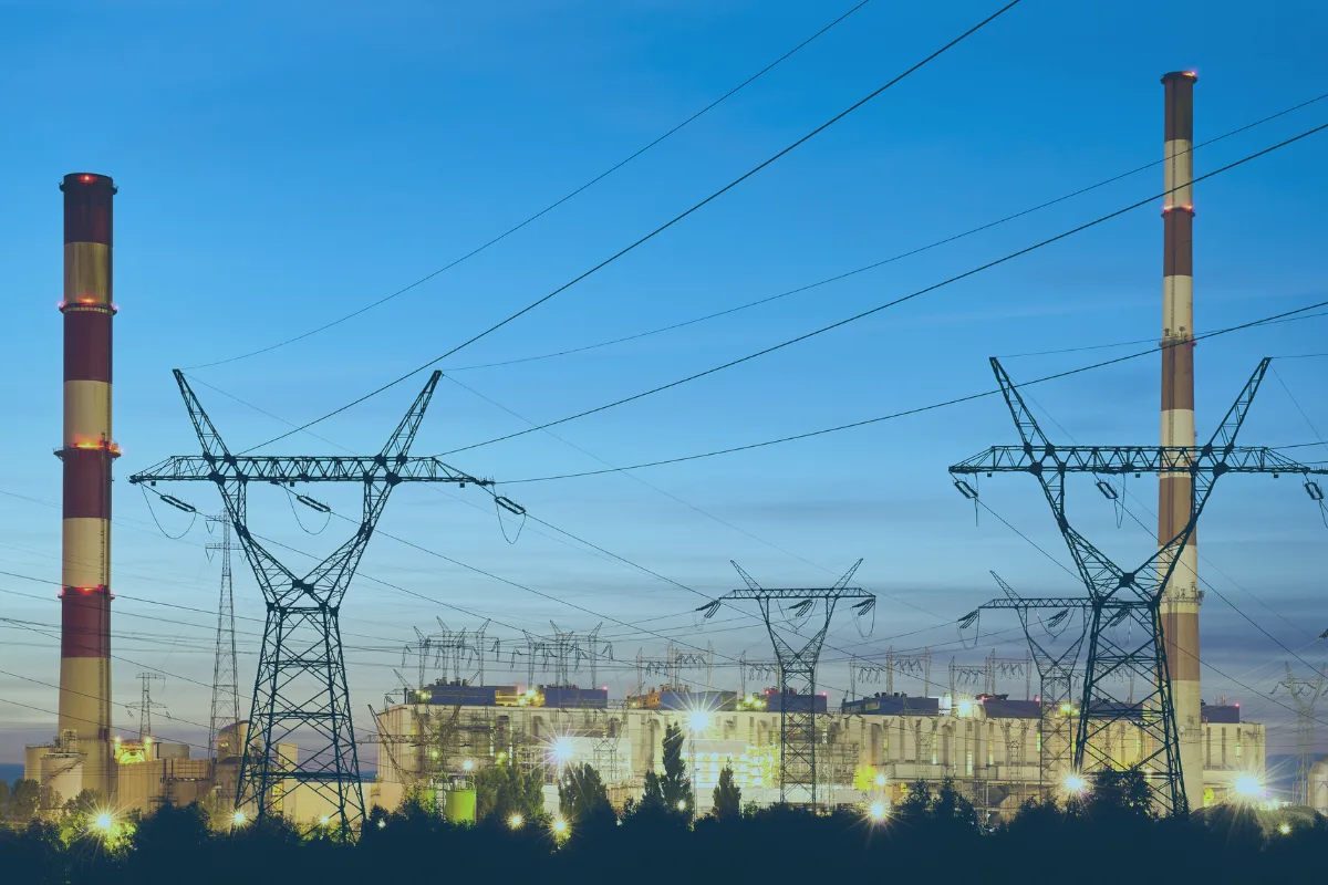 Hochspannungsmasten und Kraftwerk mit Schornsteinen in der Abenddämmerung